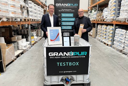 Rrene Schuch und Bürgermeister Georg Rosner stehen hinter der Testbox für Granupur in einer Lagerhalle